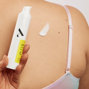 Woman holding body acne treatment bottle applying lotion on her back acne.